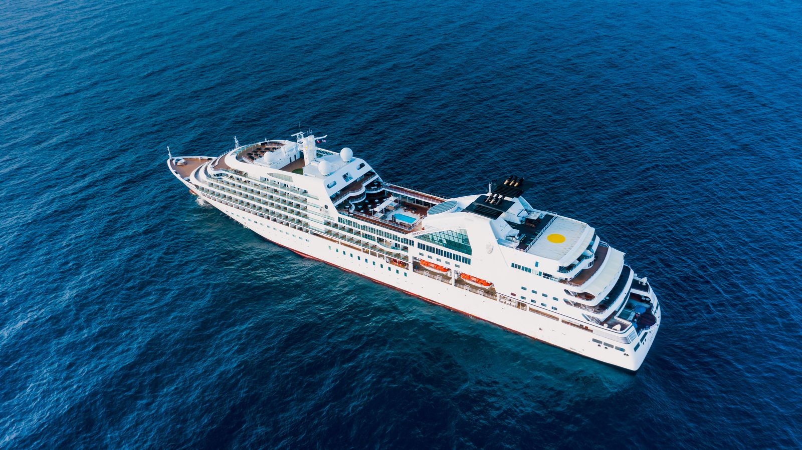 Aerial view of a full cruise ship sailing in vivid blue ocean water